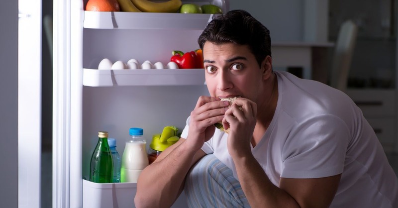 guy eating in front of the fridge in the night